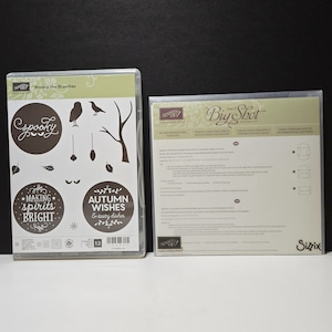 May include: A Stampin' Up! Among the Branches clear stamp set in a plastic case featuring silhouettes of an owl, a bird, a tree, leaves, and text including Spooky, Making Spirits Bright, and Autumn Wishes, next to a Sizzix Big Shot instruction sheet.