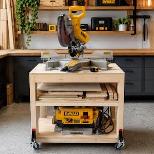 May include: A yellow and grey DeWalt mitre saw sits atop a light-coloured wooden workbench with wheels. The workbench features an open middle shelf holding wood scraps and a bottom shelf housing a yellow and grey DeWalt thickness planer.
