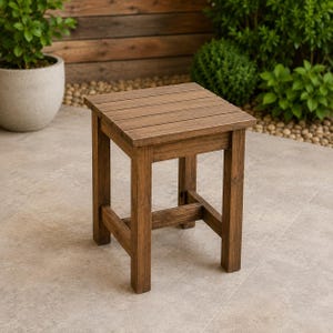 May include: A square wooden stool featuring a slatted top surface and four straight legs connected by lower support rails. The stool is constructed from dark brown wood with a visible grain pattern and has a simple, functional design.