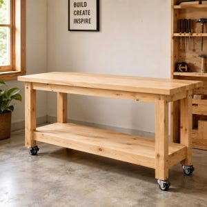 May include: A rectangular light-colored wooden workbench featuring a smooth top surface, a lower storage shelf, and four black swivel casters attached to the legs. The structure is made of natural wood with visible grain patterns throughout.