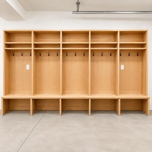 Op de afbeelding: Een grote locker van lichtgekleurd hout met vijf verticale opbergsecties. Elke sectie bevat een bovenplank, een achterpaneel met drie zwarte metalen haken en een onderste bankje met een open opbergvak eronder.