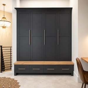 May include: A large, matte black floor-to-ceiling storage unit featuring four tall cabinet doors with long, vertical gold-toned metal handles, positioned above a bench with four drawers that have horizontal gold-toned metal pulls and a light wood top.