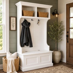 May include: A white wooden hall tree featuring an upper shelf with two woven baskets, a central panel with black metal hooks holding a dark jacket and keys, and a lower bench seat with a storage compartment, providing organized entryway storage.