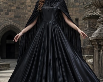 Puede incluir: Un vestido largo de satén negro con falda plisada amplia y una capa negra a juego con cuello de plumas oscuras. El conjunto se complementa con un tocado negro que presenta dos cuernos curvados, creando una estética oscura y coherente.