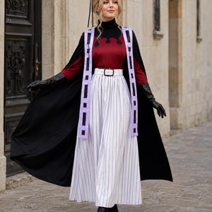 May include: A long-sleeved burgundy and black turtleneck top paired with a white pinstriped maxi skirt featuring a white belt. The outfit includes a black cape, a light purple tabard with black rectangular accents, black gloves, and a gold-trimmed headpiece.