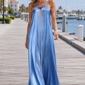 Könnte beinhalten: Ein bodenlanges Maxikleid aus hellblauem Satin mit einer lockeren, fließenden Silhouette, dünnen Spaghettiträgern und einem dekorativen Metallketten-Harnisch-Detail, das über Brust und Schultern drapiert ist und einen geschichteten Effekt erzeugt.