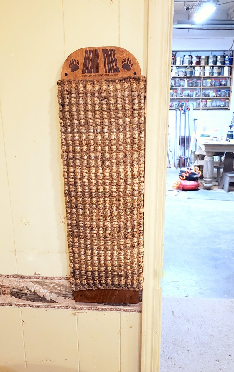 May include: A brown and tan cat scratching post with the words "BEAR TREE" and "THE ORIGINAL WALL MOUNTED SCRATCHING POST" on the top. The scratching post is mounted on a white wall.