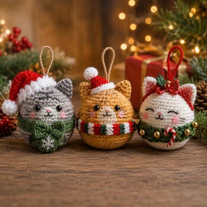 May include: Three round crocheted cat ornaments with hanging loops. The left cat is gray with a red Santa hat and green bow. The center cat is orange with a small Santa hat and striped scarf. The right cat is white with a red bow and green wreath.