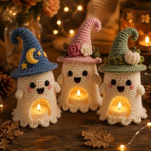 May include: Three crocheted ghost figurines, each wearing a different colored hat. The left ghost wears a blue hat with a yellow moon and stars, the center a pink hat with flowers, and the right a green hat with a white pumpkin. Each holds a tea light.