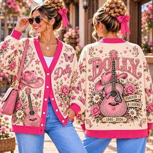 May include: A cream-colored cardigan with pink trim featuring a pink cowboy hat, acoustic guitar, roses, butterflies, and stars. The back displays the text Dolly, Forever A Legend, and 1946-2026. The front features the text Dolly.