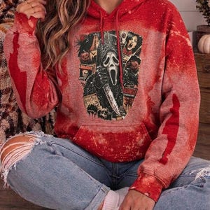 May include: A red bleached-effect hooded sweatshirt featuring a central graphic print of the Ghostface character from the Scream film franchise, holding a knife, surrounded by various horror-themed imagery and text elements on the front.
