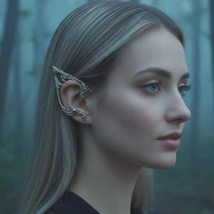 May include: A silver-toned ear cuff featuring an intricate, swirling filigree design that extends along the outer edge of the ear. The metalwork displays detailed curves and pointed tips, creating a structured, ornamental piece of jewelry.