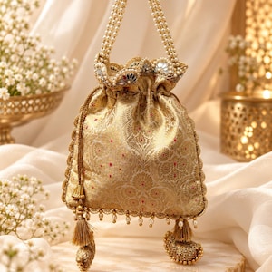 May include: A gold drawstring pouch bag featuring an intricate woven floral pattern with small red accents. The bag has a pearl-beaded handle, a scalloped top edge with mirror embellishments, and a bottom fringe with tassels and hanging pearls.