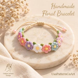 Pode incluir: Uma pulseira floral feita à mão com uma série de pequenas flores de crochê em tons pastel de rosa, roxo, azul e branco com centros amarelos, conectadas por um cordão cor de creme com duas pequenas contas rosas nas extremidades ajustáveis.