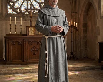May include: A floor-length grey monk robe featuring a hood, long sleeves, and a white rope belt tied at the waist with three decorative knots. A silver-toned cross pendant hangs from a chain around the neck over the fabric of the garment.