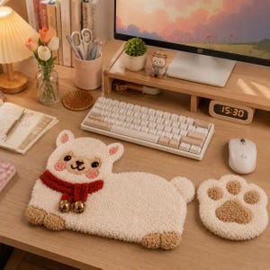 May include: A cream-colored, tufted alpaca-shaped keyboard wrist rest featuring a red scarf with two gold bells, paired with a matching cream and brown tufted paw-shaped mouse wrist rest, both made of soft, textured fabric material.