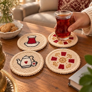 May include: Four round, cream-coloured crocheted coasters featuring embroidered designs. Two coasters display red and white tea-themed motifs, while the other two feature intricate red and gold geometric patterns with floral-like accents.