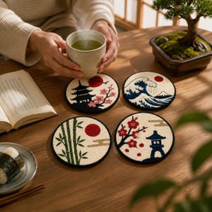 May include: Four circular coasters featuring embroidered Japanese-inspired designs, including a pagoda with cherry blossoms, a large wave, green bamboo stalks, and a stone lantern with red flowers, all set against a cream-coloured background.