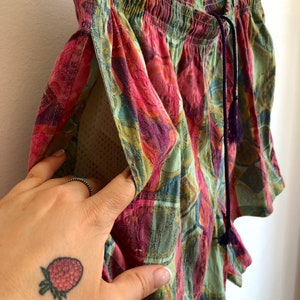 May include: Colorful patterned shorts with a drawstring waist and a small pocket. The shorts feature a vibrant mix of pink, green, and purple hues. The shorts are hanging on a wooden hanger.