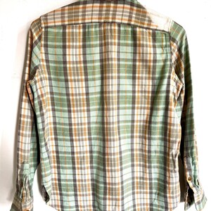 May include: A long-sleeved plaid shirt in shades of green, brown, and white. The shirt features a button-down collar and cuffs. The back of the shirt is visible, showcasing the plaid pattern.