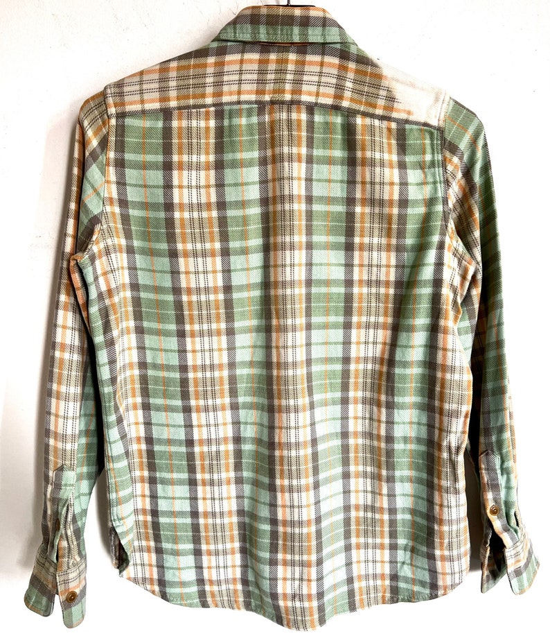 May include: A long-sleeved plaid shirt in shades of green, brown, and white. The shirt features a button-down collar and cuffs. The back of the shirt is visible, showcasing the plaid pattern.