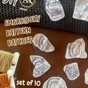 Puede incluir: Un conjunto de 10 parches adhesivos con patrones de bordado que presentan varios diseños dibujados a mano en tinta morada sobre tela estabilizadora blanca, junto a dos carretes de hilo de bordar beige y naranja.