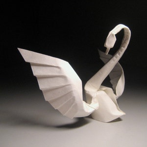 Puede incluir: Un cisne de origami blanco con el cuello curvado hacia atrás y las alas extendidas. El cisne está hecho de papel y es una forma de arte tradicional japonesa.