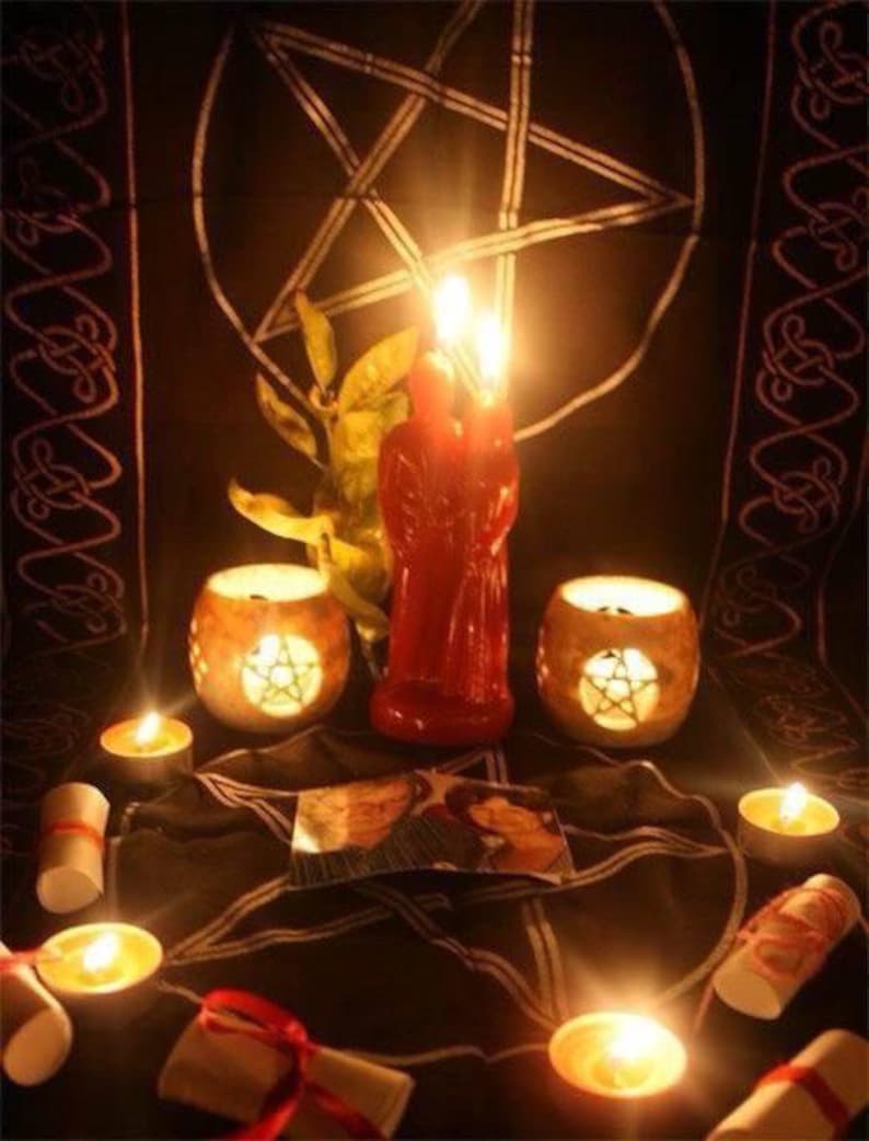 May include: A ritual setup featuring a black cloth with a white pentagram, a red dual-figure candle, two stone candle holders with pentagram cutouts, several tea light candles, and rolled paper scrolls tied with red ribbon, all illuminated by warm light.