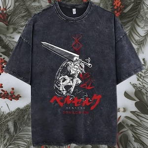 Puede incluir: Una camiseta gris carbón con efecto lavado al ácido que presenta un gráfico en blanco y rojo de un guerrero sosteniendo una gran espada. Sobre la figura hay un símbolo rojo y debajo el texto japonés rojo "ベルセルク" con "BERSERK" debajo.