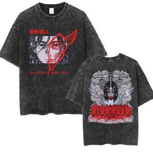 Könnte beinhalten: Ein anthrazitfarbenes T-Shirt in Acid-Wash-Optik mit einer Grafik auf der Vorderseite, die ein Gesicht mit roter Umrandung und japanischem Text zeigt. Die Rückseite zeigt eine detaillierte Illustration einer zentralen Figur mit Rauch.