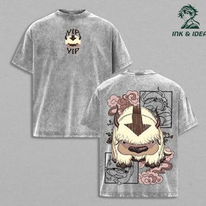 May include: A grey acid-wash t-shirt featuring a small graphic on the front with the text YIP YIP and a stylized creature head. The back displays a large illustration of a furry creature with horns, surrounded by pink clouds and line art.