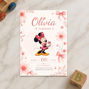 May include: A rectangular birthday invitation card featuring a pink watercolour floral border with bows and a central illustration of Minnie Mouse holding a gift. The text reads Olivia IS TURNING 3, MONDAY 09 SEPTEMBER, 1-3 PM, 123 Anywhere St, Any City.