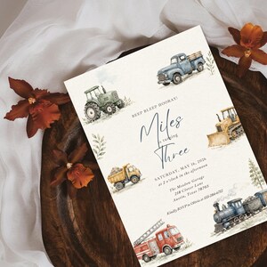 May include: A rectangular birthday invitation card featuring watercolor illustrations of a blue pickup truck, green tractor, yellow bulldozer, dump truck, red fire engine, and a steam train. The text reads BEEP BLEEP HOORAY! Miles is turning THREE, SATURDAY, MAY 16, 2026, at 2 o'clock in the afternoon, The Meadow Garage, 218 Clover Lane, Austin, Texas 78703, Kindly RSVP to Olivia at 555-284-6712.