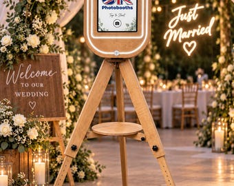 May include: A wooden photo booth kiosk mounted on a tripod stand with an integrated tablet display. The screen shows the text UK Photobooth and Tap to Start. The oval-shaped head unit features a glowing white LED ring light around the tablet screen.