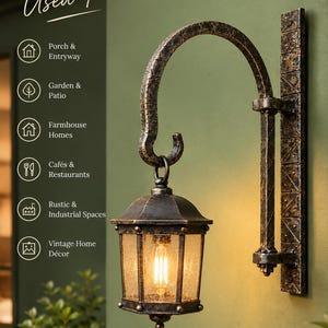 Könnte beinhalten: Eine Wandlaterne mit dunkel patiniertem Bronzefinish und einem geschwungenen, texturierten Metallarm. Der sechseckige Glasschirm enthält eine warm leuchtende Edison-Glühbirne. Der Text links lautet: Used For, Porch & Entryway, Garden & Patio, Farmhouse Homes, Cafés & Restaurants, Rustic & Industrial Spaces, Vintage Home Décor.
