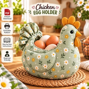 Puede incluir: Un porta huevos de tela con forma de gallina, con un estampado floral de margaritas blancas y amarillas sobre un fondo verde salvia. La gallina tiene una cresta y barbillas de color naranja brillante, un ojo negro y una cola con volantes.