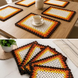 Op de afbeelding: Een set rechthoekige gehaakte placemats met een granny square patroon met concentrische lagen van wit, geel, oranje en donkerbruin garen. De placemats hebben een geschulpte rand en zijn gestapeld of op een houten tafel geplaatst.