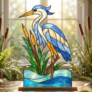 May include: A stained glass panel featuring a blue and white heron standing among green reeds and brown cattails in blue water. The piece is mounted on a wooden base and includes the text Polaris Glass Studio printed on the bottom right corner.