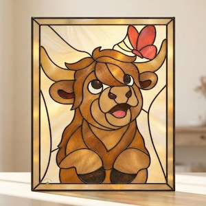 May include: A rectangular stained glass panel featuring a brown Highland cow with a red butterfly perched on its horn. The cow has large dark eyes and a light brown muzzle. The background consists of cream-colored glass pieces with dark lead lines.