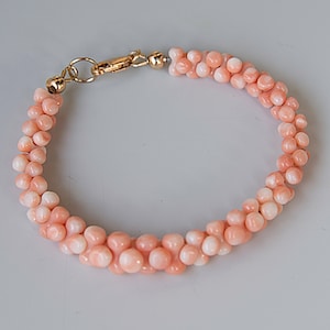 May include: A delicate pink coral bracelet with a gold clasp. The bracelet is made of small, round beads that are strung together in a double row.