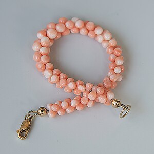 May include: A pink coral beaded bracelet with gold clasps. The bracelet is made of small, round beads that are strung together in a double strand.
