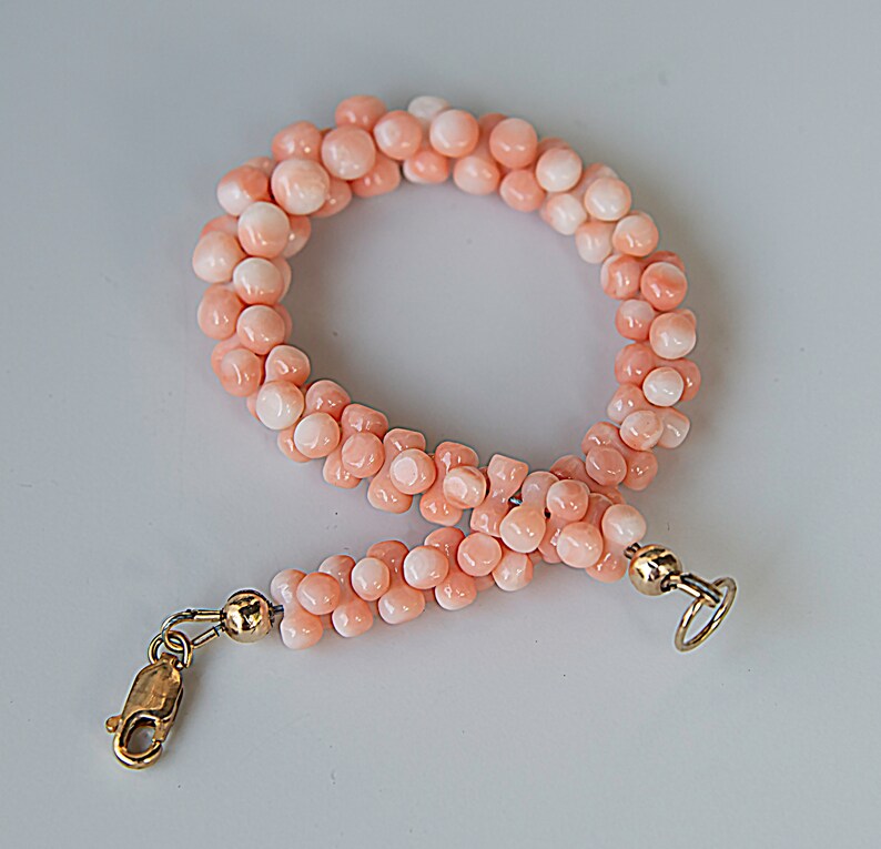 May include: A pink coral beaded bracelet with gold clasps. The bracelet is made of small, round beads that are strung together in a double strand.