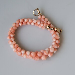 May include: A delicate pink coral bracelet with a gold clasp. The bracelet is made of small, round beads and is perfect for a casual or formal occasion.