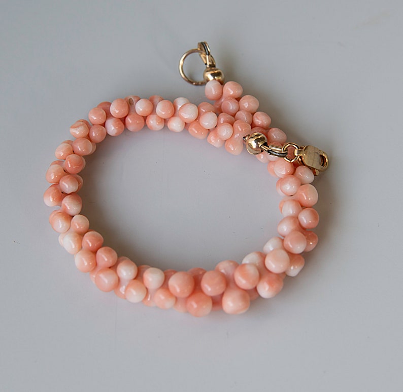 May include: A delicate pink coral bracelet with a gold clasp. The bracelet is made of small, round beads and is perfect for a casual or formal occasion.