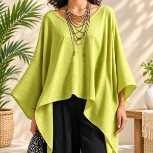 May include: A lime green V-neck poncho top with wide, flowing sleeves and a high-low hemline. The garment is paired with a multi-layered gold-toned necklace featuring several thin chains and a black patterned accessory held at the side.