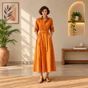 May include: A long-sleeved, button-down midi dress in a solid burnt orange color. The dress features a collared neckline, a matching fabric belt with a rectangular buckle at the waist, and a full, flowing skirt that reaches below the knees.