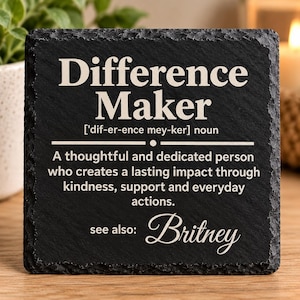 May include: A square black slate coaster with rough, textured edges featuring white engraved text that reads: Difference Maker ['dif-er-ence mey-ker] noun. A thoughtful and dedicated person who creates a lasting impact through kindness, support and everyday actions. see also: Britney.