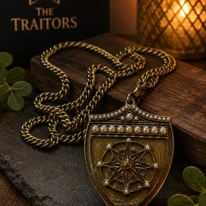 Puede incluir: Un collar con colgante de metal en tono lat&oacute;n que presenta un dije en forma de escudo con un dise&ntilde;o de rosa de los vientos en relieve. El escudo est&aacute; decorado con peque&ntilde;as perlas blancas en el borde superior y en los puntos cardinales.