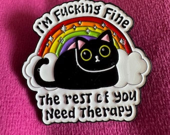 Puede incluir: Un pin de esmalte negro que muestra un gato negro sentado frente a un arcoíris y nubes blancas. El texto en la parte superior dice I'M FUCKING FINE y el texto en la parte inferior dice The rest of you Need Therapy. Incluye pequeñas estrellas plateadas.
