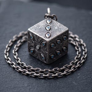 May include: A silver cube pendant on a matching chain, featuring an intricate textured surface with engraved floral patterns and small, embedded blue gemstones arranged in eye-like shapes across the faces of the cube.